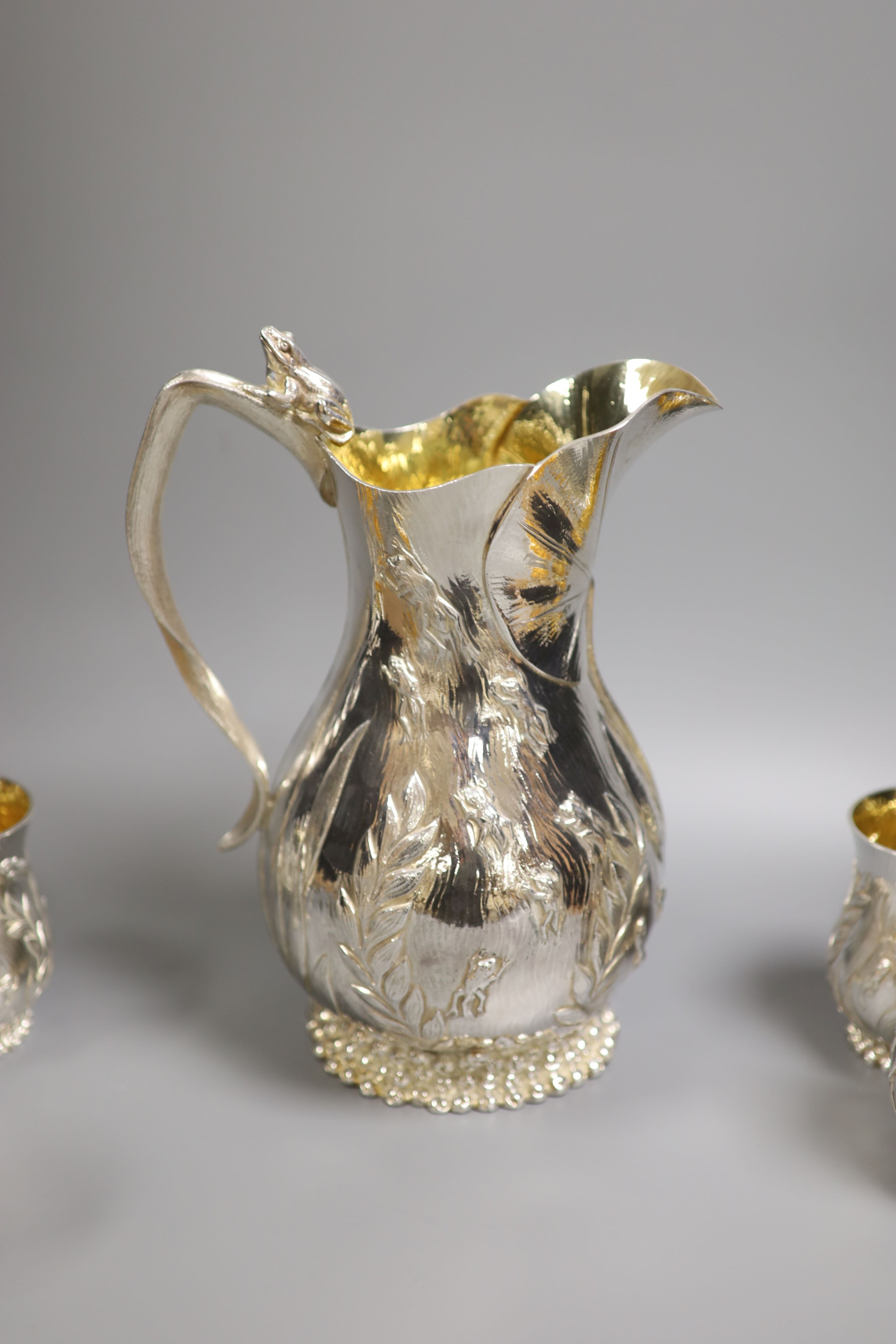 A good set of six Garrard & Co Ltd silver mugs and a matching jug, London, 1997, all embossed with frogs spawn amongst reeds, with gilded interiors, jug height 27.1cm